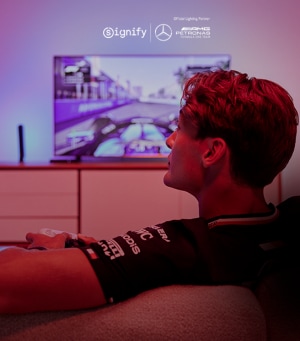 Der Formel-1-Fahrer George Russell sitzt auf einer Couch vor dem Fernseher und spielt ein Rennspiel.