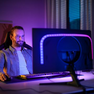 Ein Mann sitzt vor einem PC-Monitor, der mit einem Hue-Lichtstreifen ausgestattet ist, der in blauen und violetten Farbtönen leuchtet.